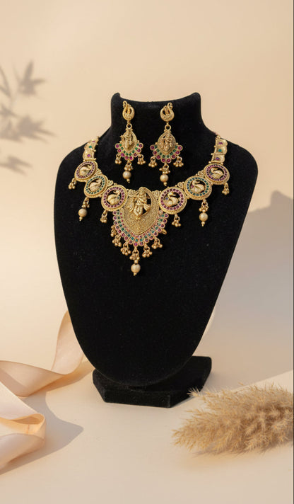 Ornate gold necklace and earrings set on a black stand with a blue background