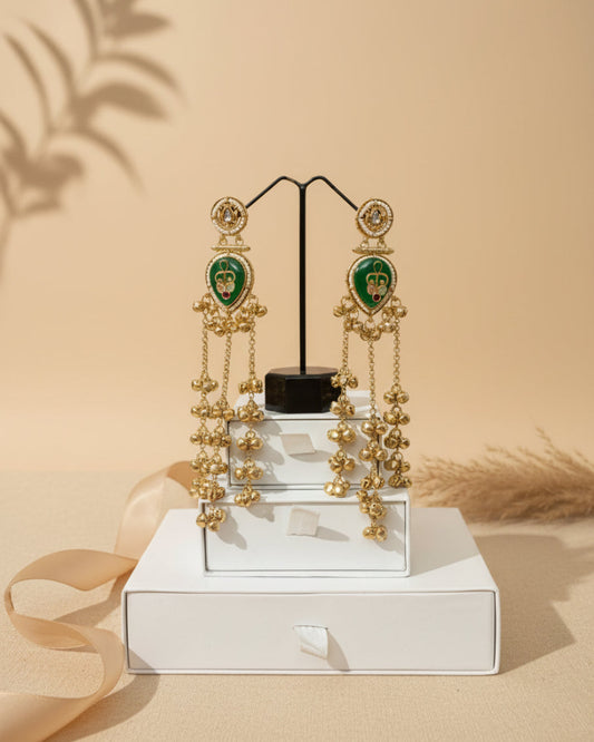Gold earrings with green gemstones on a white box against a black leather background