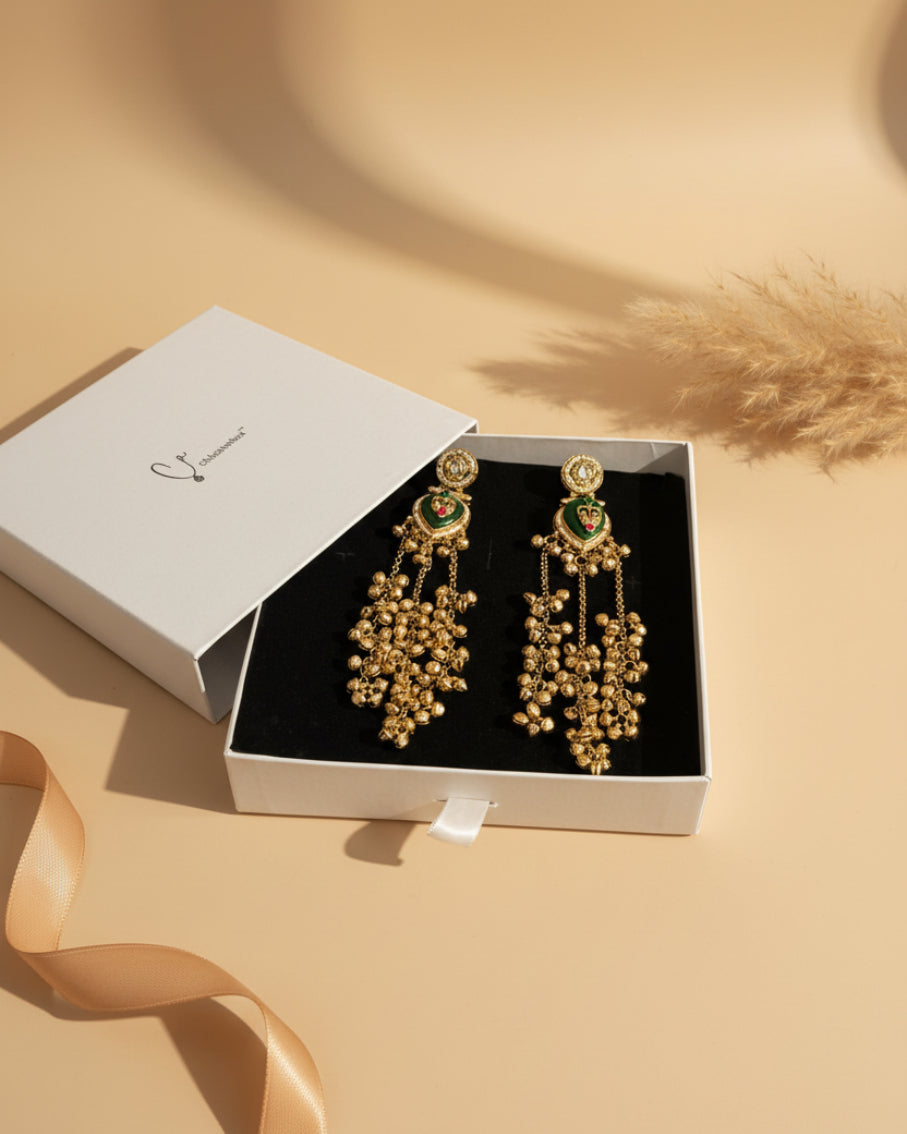 Gold earrings with green accents in a white box on a red surface.