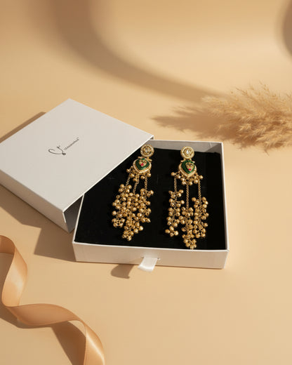 Gold earrings with green accents in a white box on a red surface.