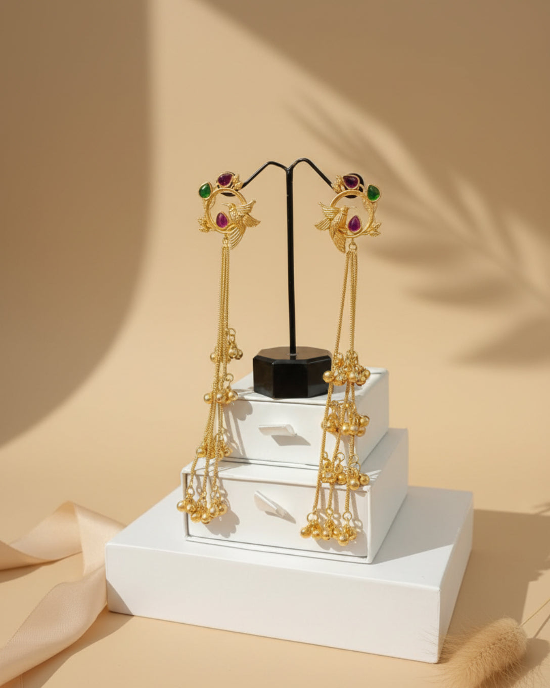 Gold earrings with gemstones on a white stand against beige background