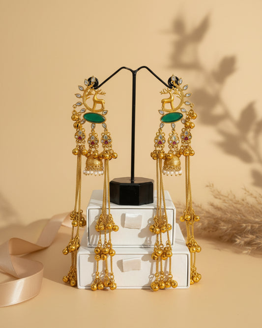 Pair of long gold-plated Kashmiri brass Dehjoor jhumka earrings featuring emerald green teardrop stones and cascading ghungroo bell tassels.