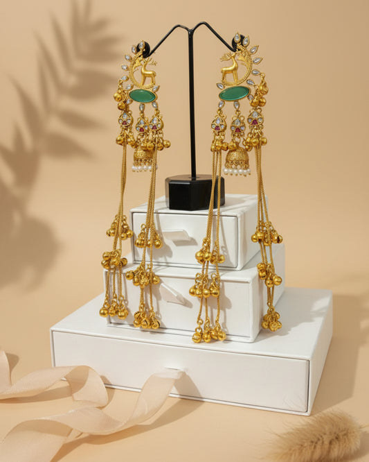 Gold earrings with green gemstones on a white stand against a beige background