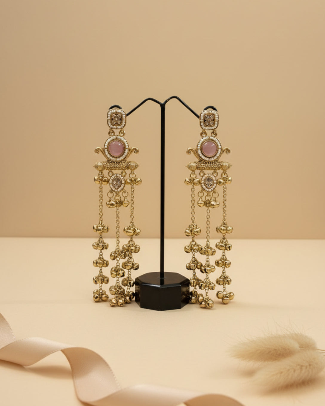 Pair of long gold-plated Kashmiri brass Dehjoor jhumka earrings featuring ruby pink teardrop stones and cascading ghungroo bell tassels.