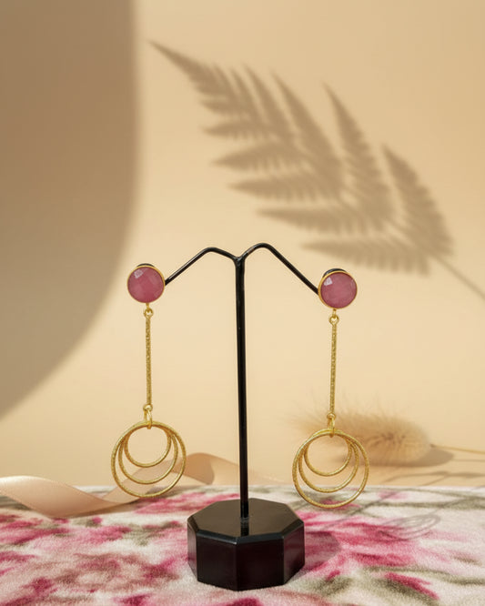 Handcrafted brass drop earrings featuring a round ruby pink gemstone stud and a dangling triple-layered textured gold-tone hoop design.