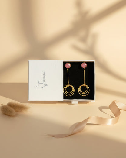 Gold hoop earrings with pink stones in a branded box on a patterned fabric background