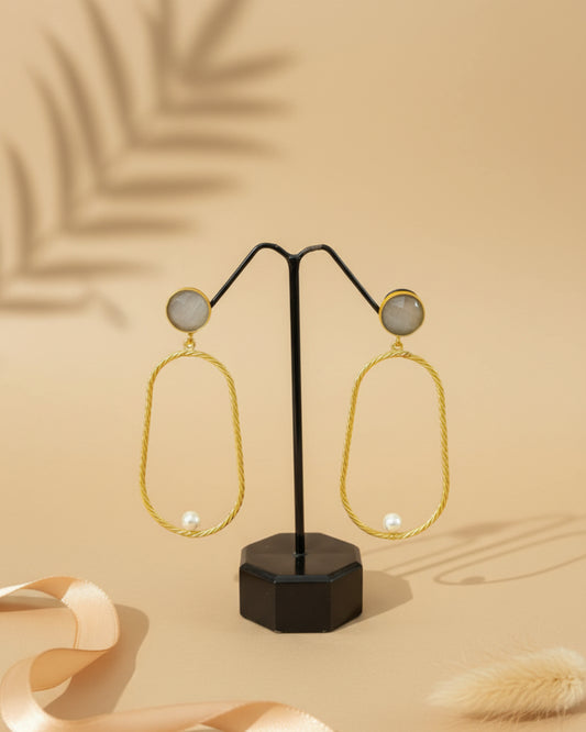 Handcrafted brass drop earrings featuring a round grey stone stud and a large twisted gold-tone oval hoop accented with a single white pearl.