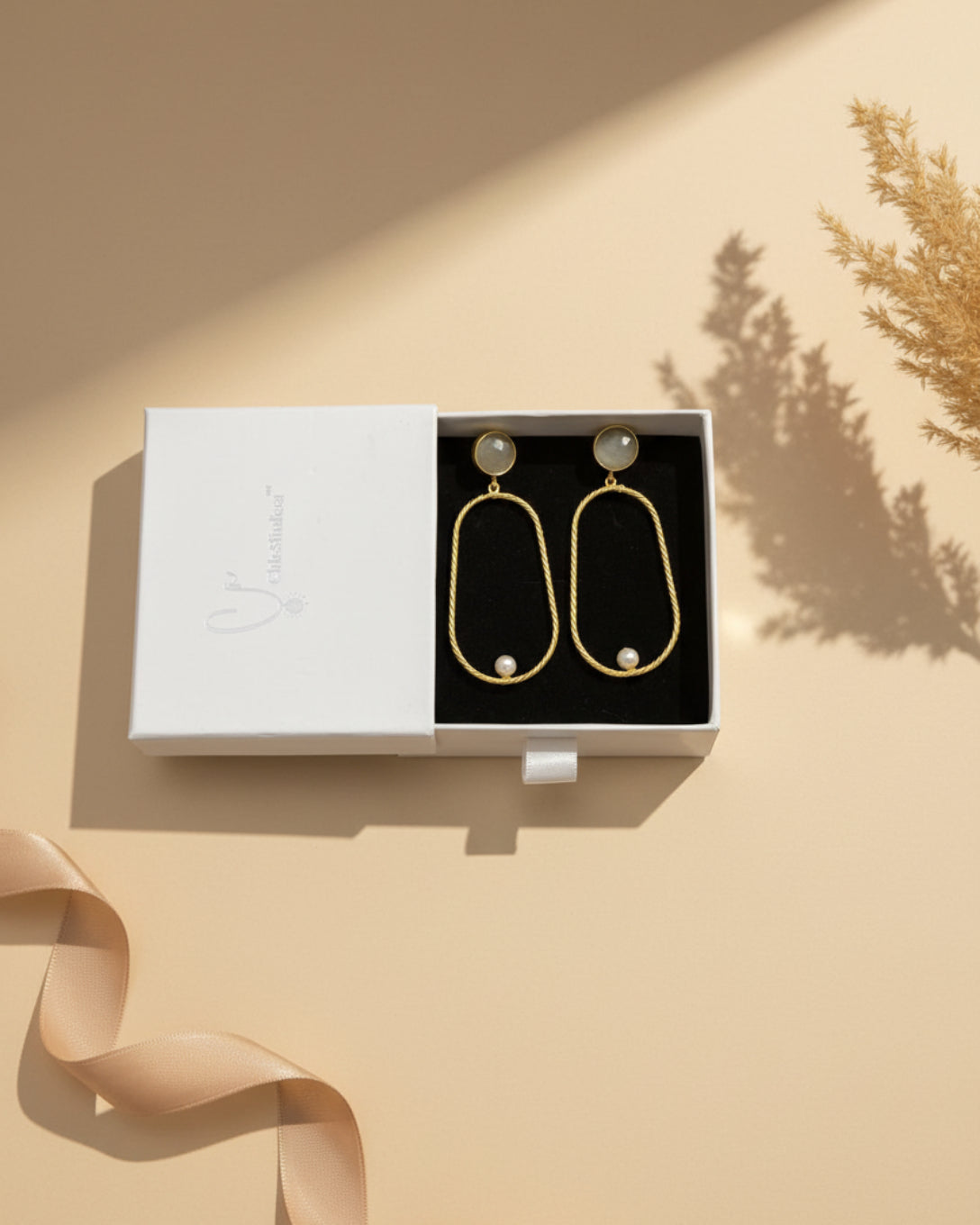 Gold earrings with pearls on a branded box against a floral background