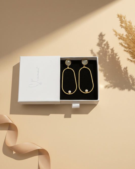 Gold earrings with pearls on a branded box against a floral background