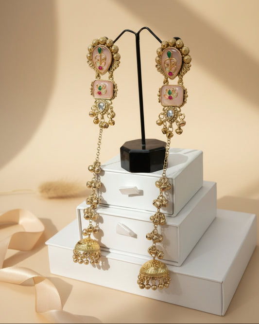 Ornate gold earrings with gemstones on a stand against a dark background