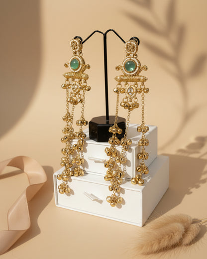 Gold earrings with green gemstones on a stand against a black leather background