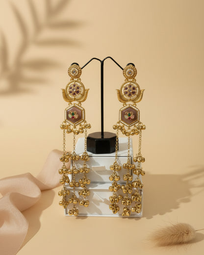 Gold earrings with intricate designs on a stand against a black leather background.