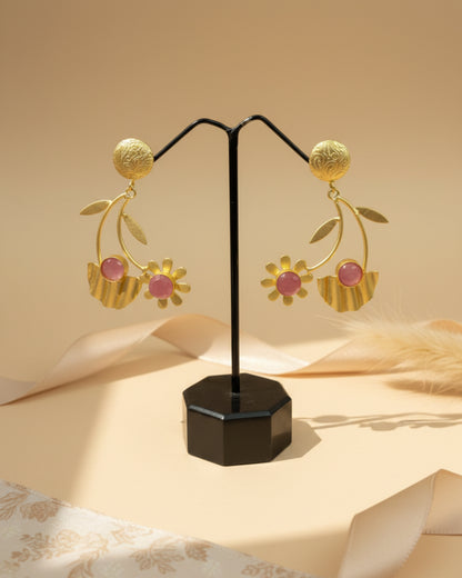 Handcrafted matte gold-plated brass drop earrings featuring a whimsical floral branch design with rose pink stone accents and textured leaf details.