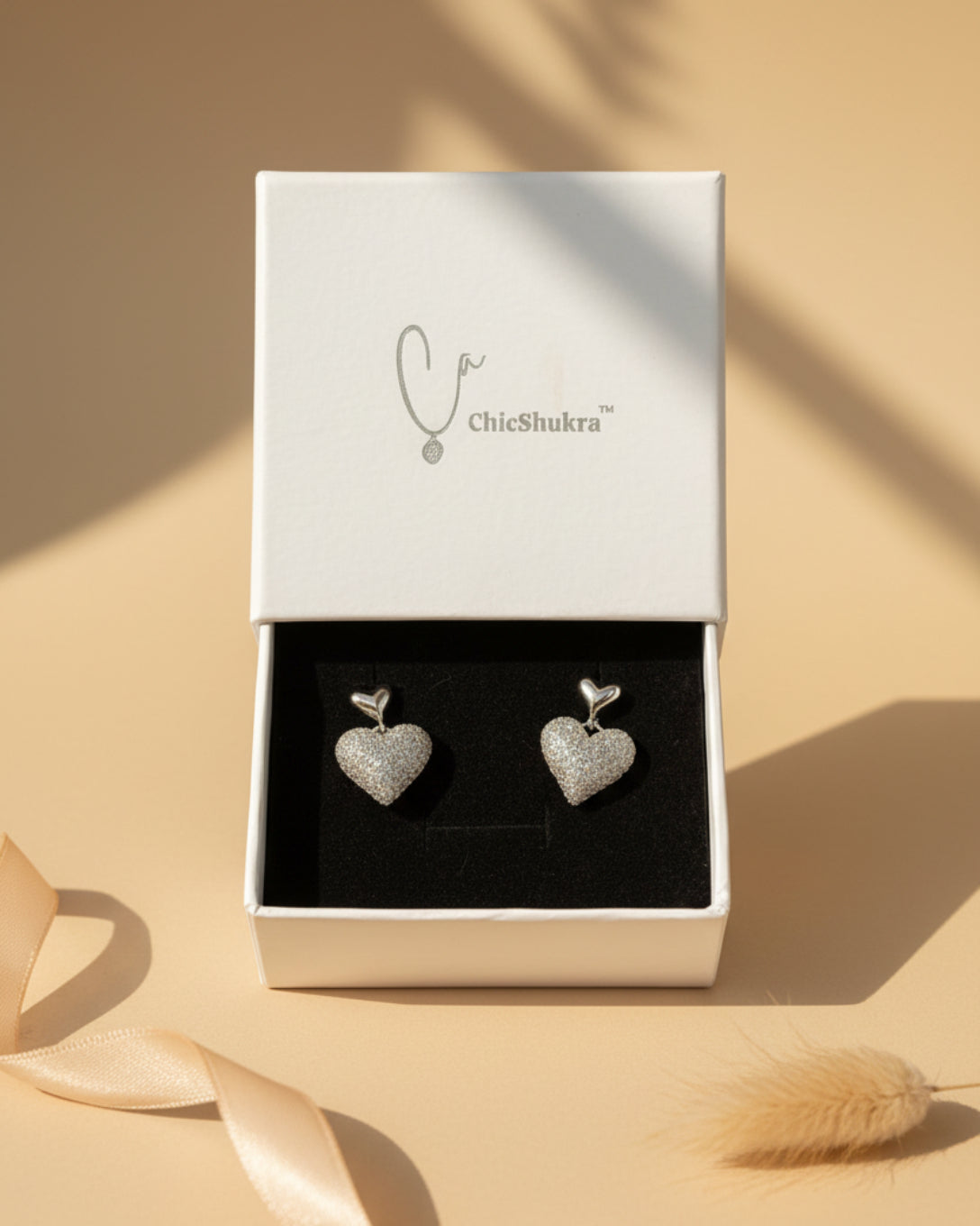 Heart-shaped earrings in a ChieShukra box on a patterned fabric background