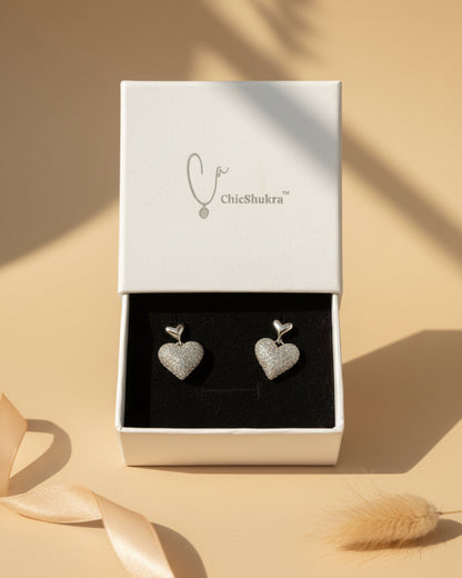 Heart-shaped earrings in a ChieShukra box on a patterned fabric background