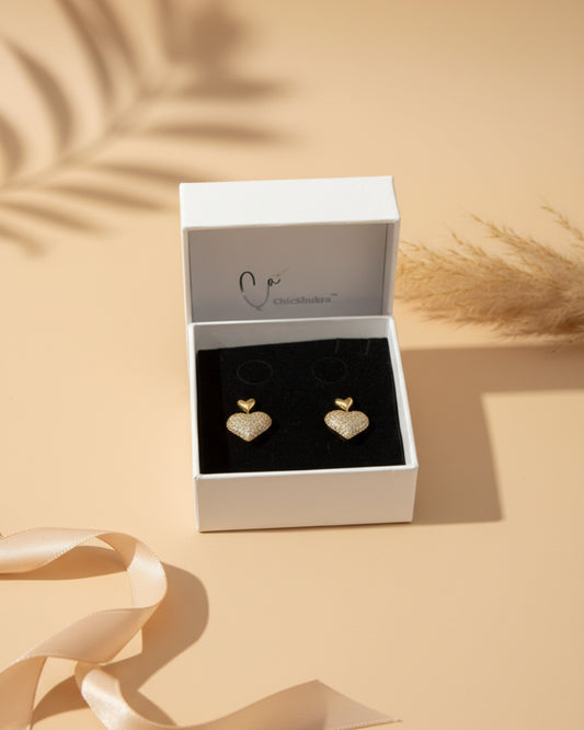 Heart-shaped gold earrings in a Clogau box on a patterned surface