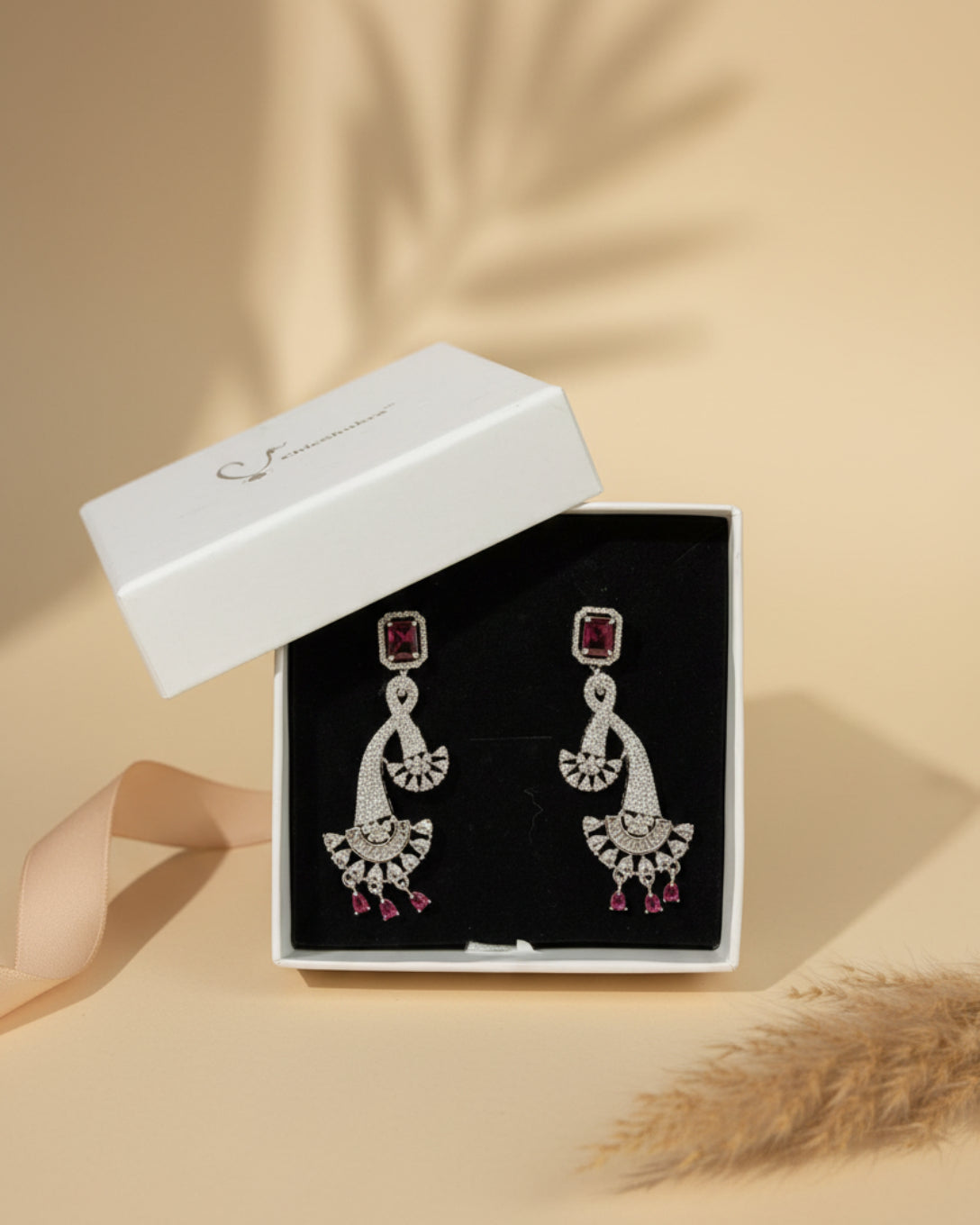 Silver earrings with red gemstones in a box with 'Chic Shukra' branding on a floral fabric background.