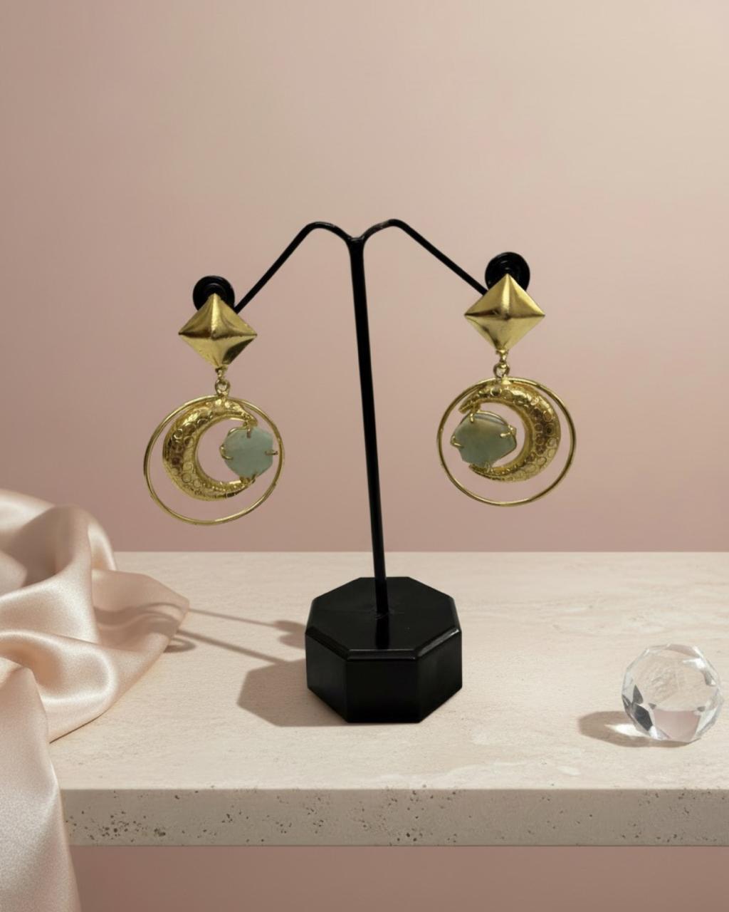 Gold earrings on a black stand against a pink background