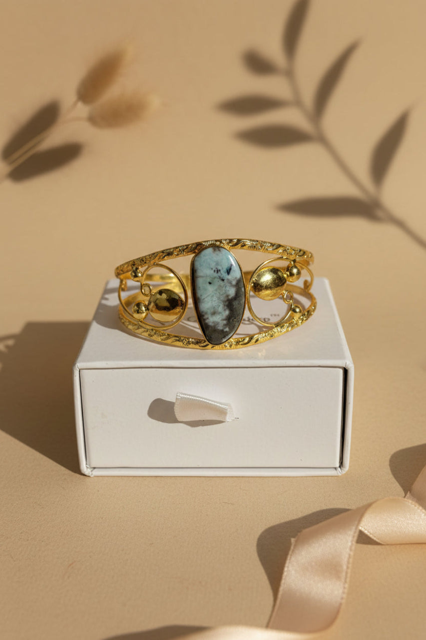Gold bracelet with a central blue stone on a white box against a beige background