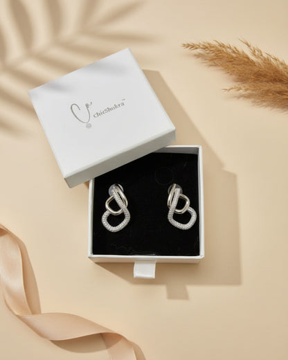 Silver earrings in a box with 'chicshukra' branding on a floral-patterned fabric background.